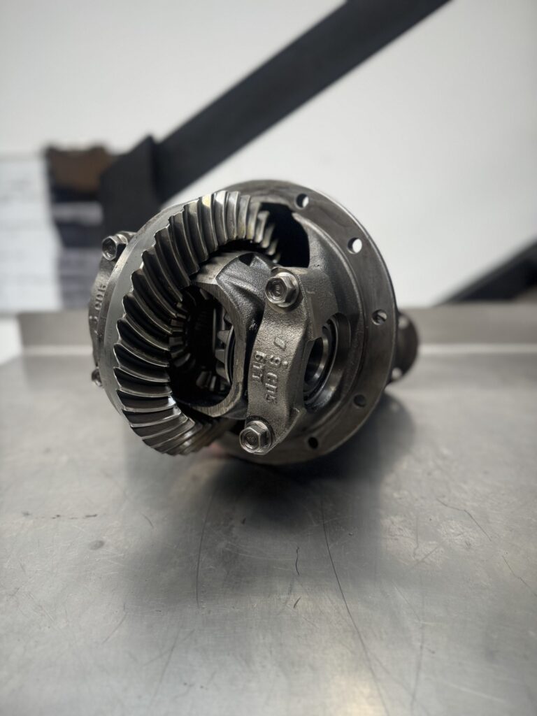 A close-up of the Import placeholder for 1804 metal differential gear assembly on a metallic surface, highlighting detailed gear teeth and components, with a blurred workshop in the background.