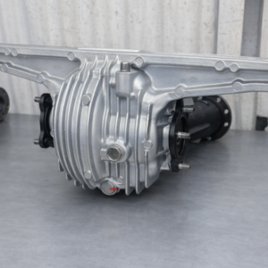 A Mazda RX7 FC Rebuilt Rear Differential 4.1 Ratio Open is shown on a grey surface against a corrugated wall, featuring a ribbed casing, circular cover, and axles extending from both sides.