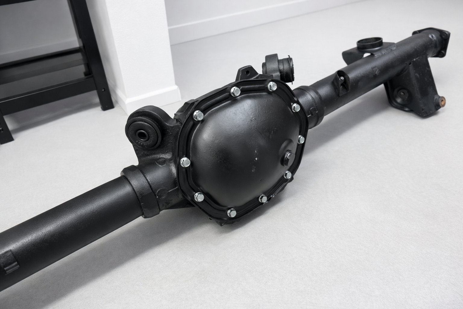 A Holden HQ Rebuilt Rear Diff 3.36 Ratio LSD, black in colour, sits on a light grey floor, featuring visible bolts around the cover and axle tubes extending from both sides.