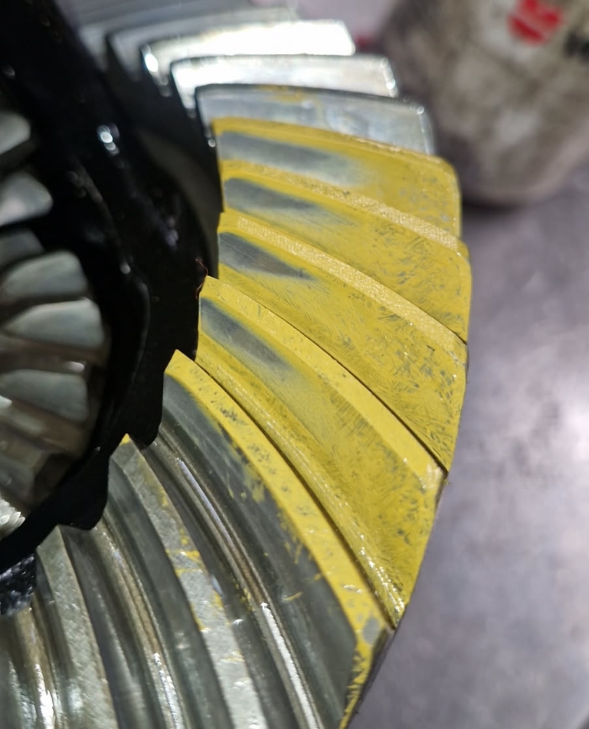Close-up of a metal gear with yellow marking compound applied to the teeth, for checking gear contact patterns.