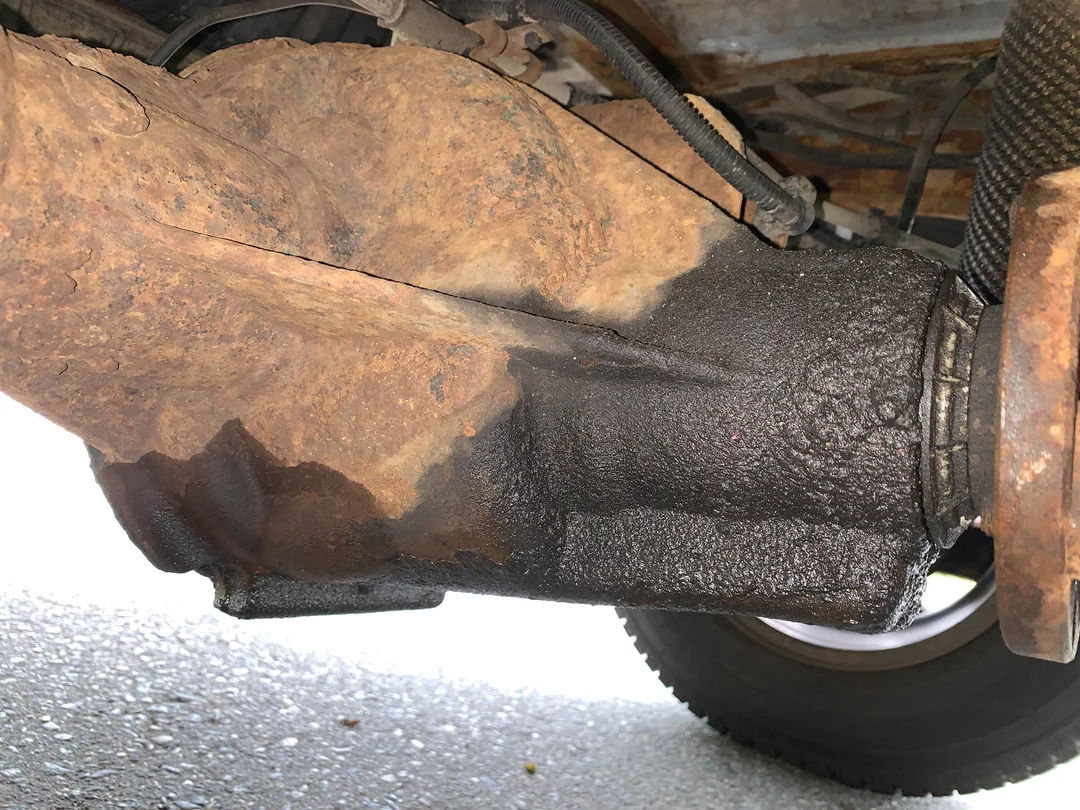 Close-up of a vehicle's rusty differential with a noticeable oil leak and wet, dark stains on the metal surface, showing signs of wear and possible maintenance needs.