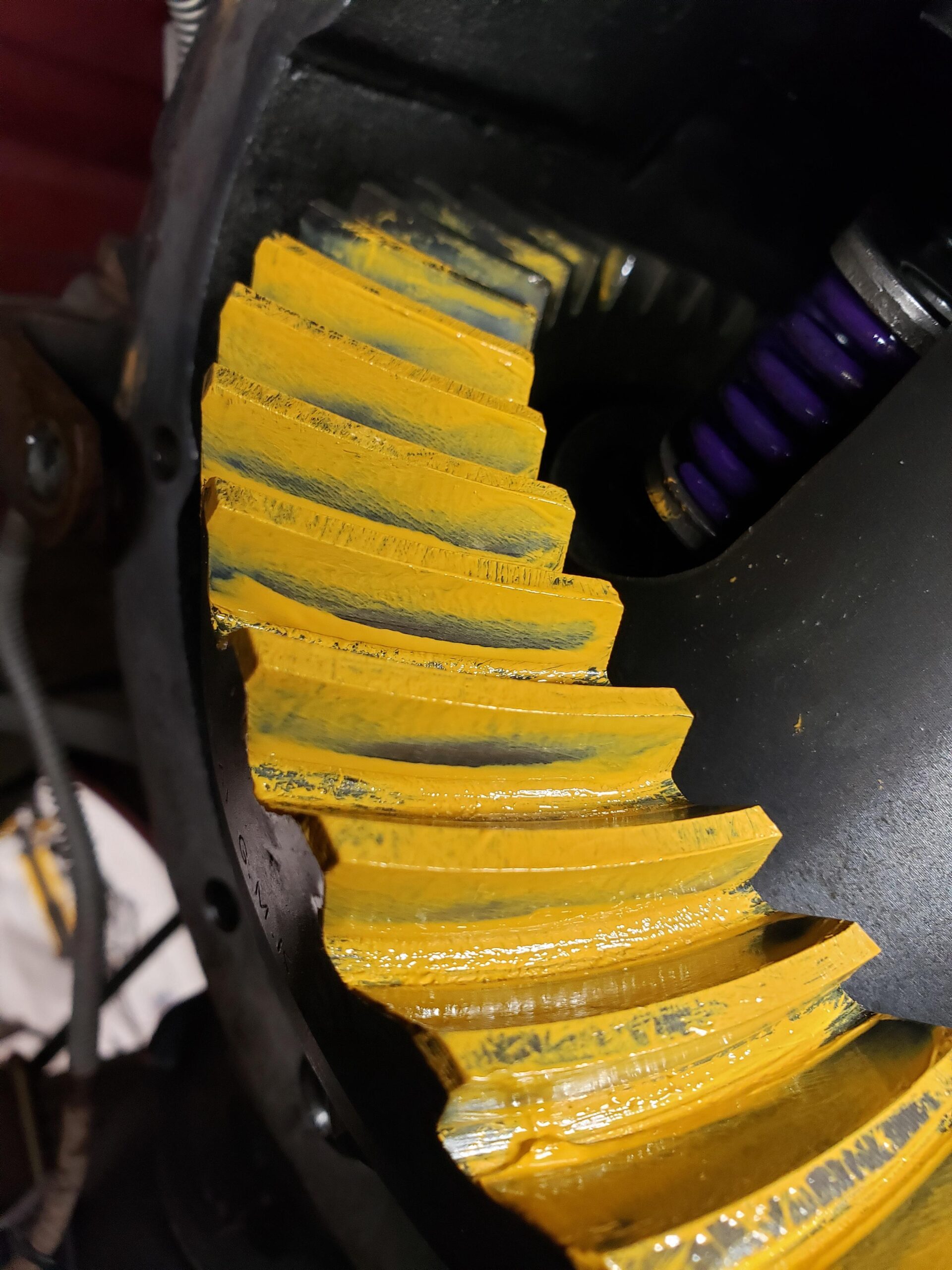 Close-up of a gear inside a differential, coated with yellow marking compound to check the contact pattern between the gear teeth. The metal gears show signs of wear and use.