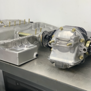A Nissan Skyline GT-R R32/R33/R34 Front & Rear 4.625 Diff Package with Cusco LSDs, featuring a shiny metal differential with bolts and gears, is placed on a grey workbench against a plain light-coloured wall.