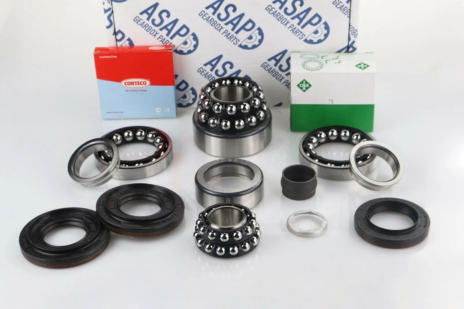 A variety of ball bearings, oil seals, and automotive parts are arranged neatly on a white surface, with branded boxes labelled ASAP, CORTECO, and others in the background.