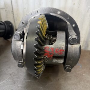 A close-up of a Ford Courier 4WD 4.44 LSD Rebuilt Rear Exchange Diff, featuring yellow markings on the gear teeth and red markings on the casing, placed on a brown surface in front of a corrugated metal wall.