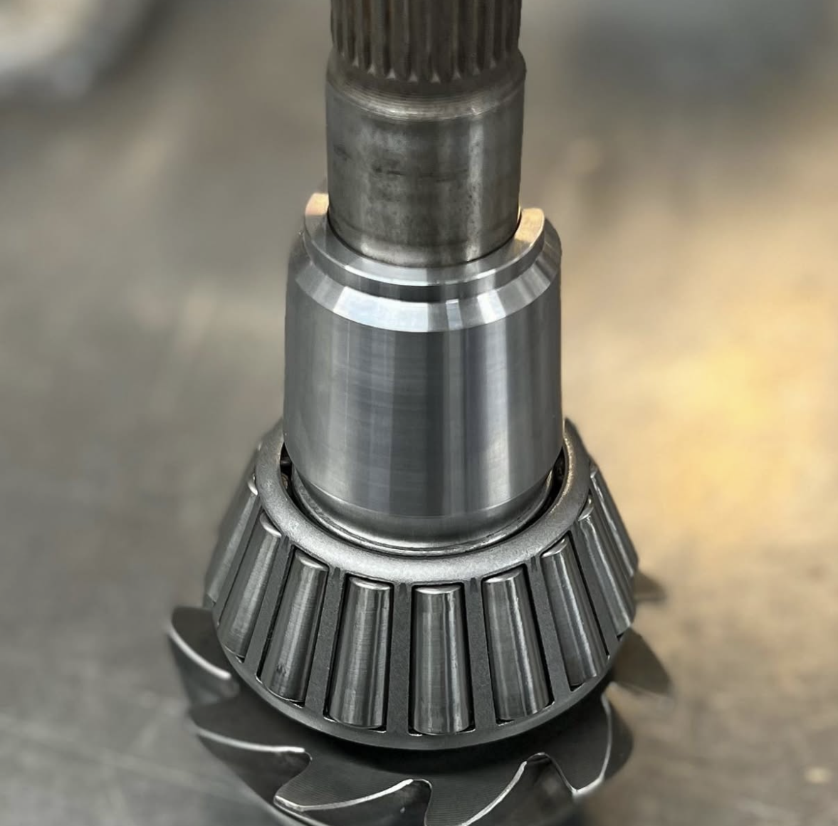 Close-up of a metal gear component featuring a shiny, smooth cylindrical shaft and angled teeth—complete with Solid Pinion Spacers. Photographed on a light surface. Instagram post by gearhead_diffs in Christchurch, New Zealand.