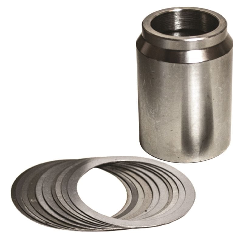 A solid pinion spacer stands upright next to a fanned-out stack of thin, circular metal shims, all placed on a white background.